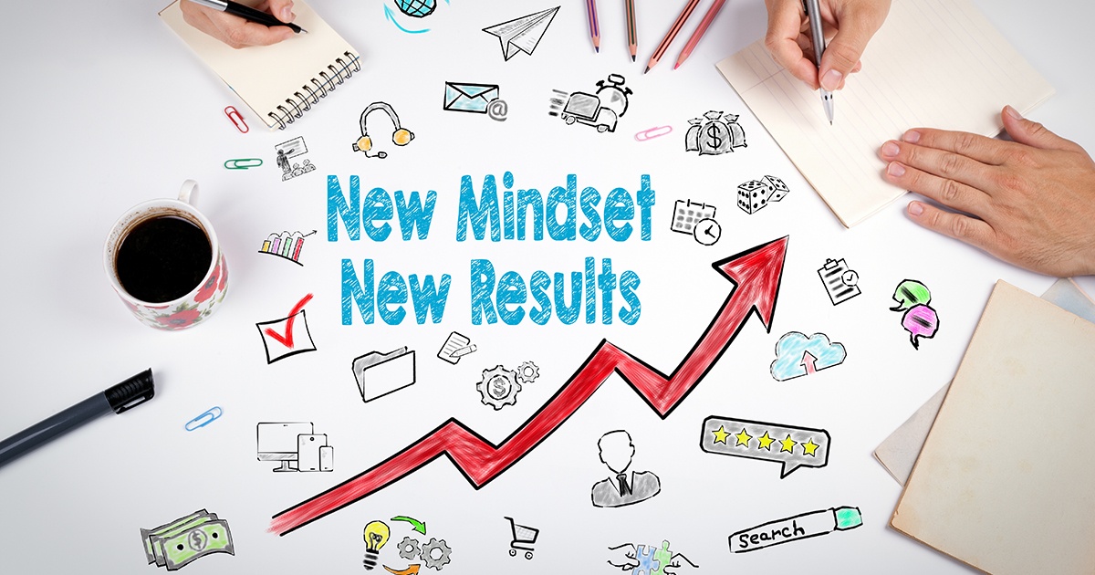 A motivational workspace scene featuring the phrase &ldquo;New Mindset New Results&rdquo; written in bold blue text. Surrounding the words are colorful hand-drawn doodles representing business and productivity &mdash; such as gears, money, a calendar, speech bubbles, a magnifying glass, and a five-star review bubble. A red upward arrow runs through the center, symbolizing growth and progress. On the sides, a person&rsquo;s hands are shown writing on notepads, with coffee, pens, and paperclips completing the creative desk setup.