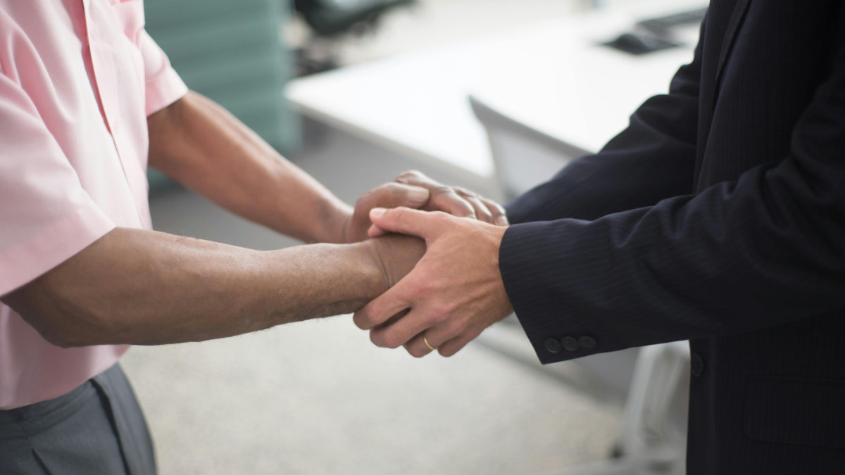 Two people standing and holding each other&rsquo;s hands in a supportive, reassuring gesture in an office setting.