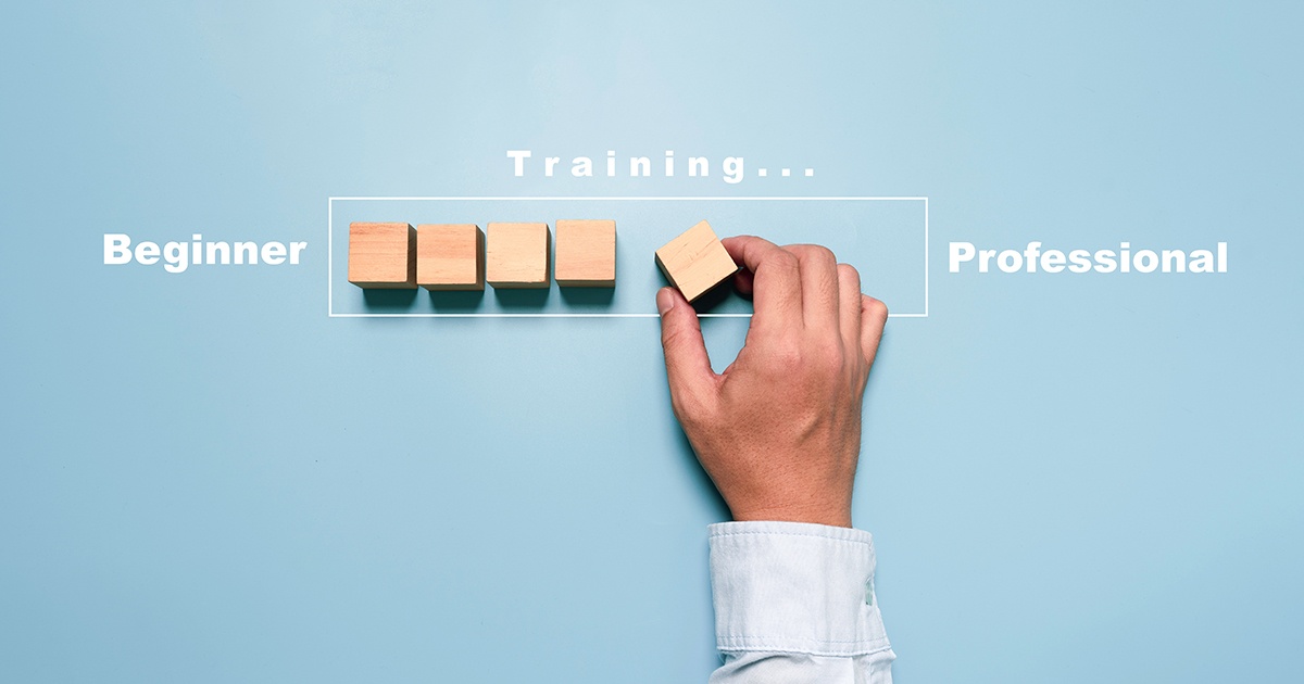 Hand placing the final wooden block in a row between the words “Beginner” and “Professional,” illustrating the journey from beginner to professional through training.